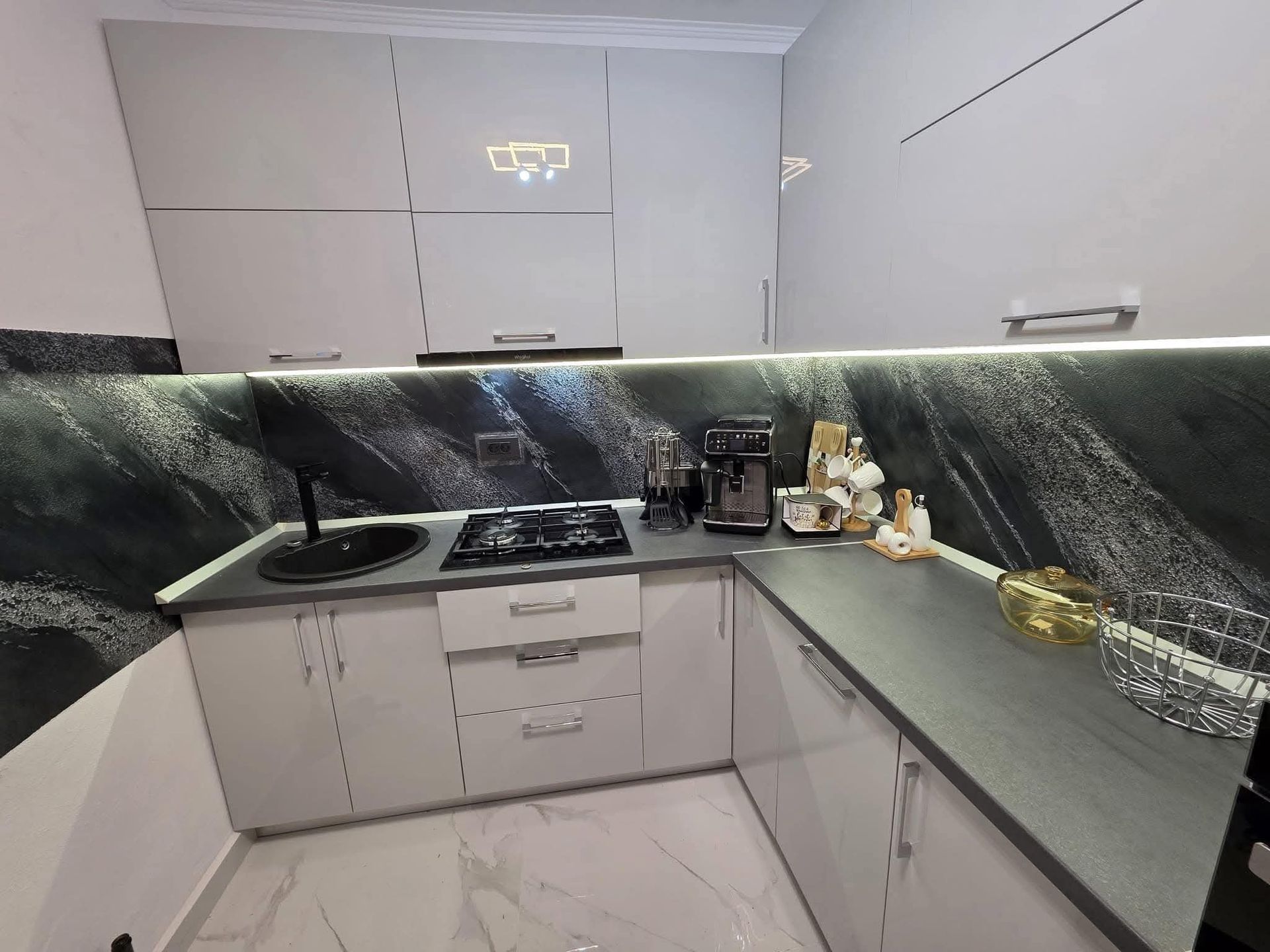 Cucina moderna bianca con paraschizzi, lavello, piano cottura ed elettrodomestici in marmo nero.