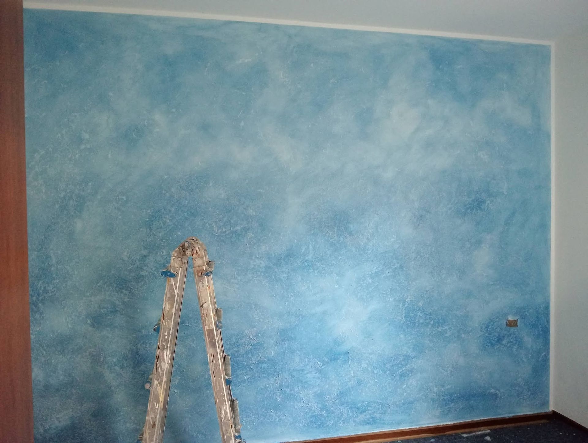 In una stanza in fase di ristrutturazione, una parete blu con una scala appoggiata ad essa è disposta a mo' di muro.