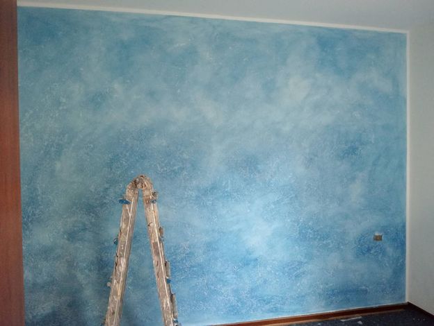 Muro dipinto di blu con una scala appoggiata e una piccola macchia di vernice sulla destra.