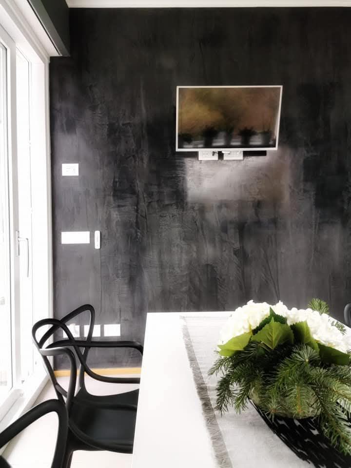Sala da pranzo moderna con parete d'accento nera, TV a parete e tavolo con centrotavola di piante.