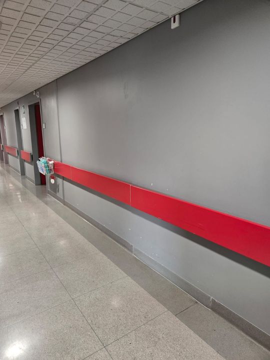 Corridoio interno vuoto con pareti grigie, una striscia rossa sulla parete e pavimento lucido.