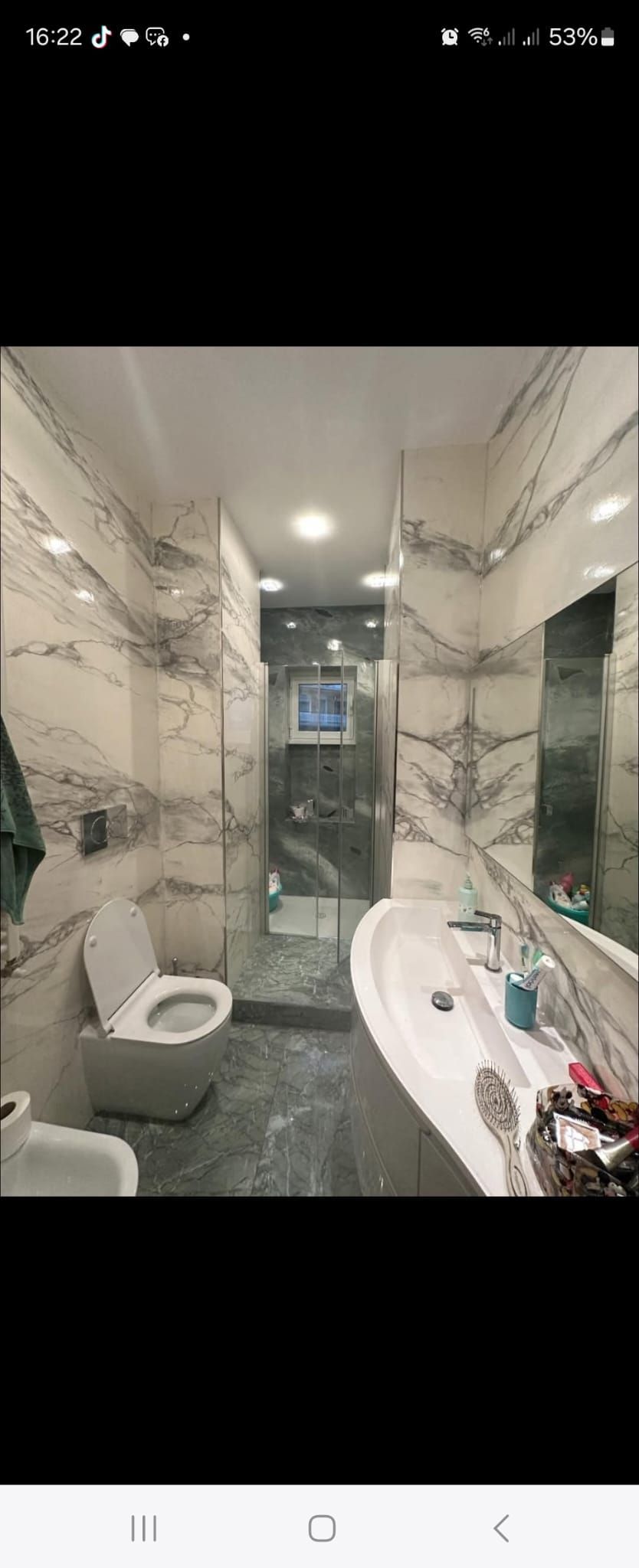 Bagno stretto piastrellato con WC, lavandino, specchio a parete e plafoniera.