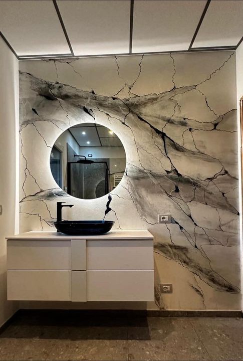 Mobile bagno moderno con specchio rotondo retroilluminato e parete con motivo marmorizzato.