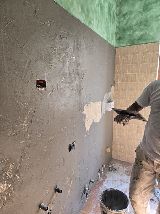 Un operaio applica l'intonaco a una parete grigia in una stanza in fase di ristrutturazione.