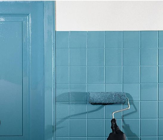 Rullo da pittura che applica vernice blu su una parete piastrellata accanto a una porta blu