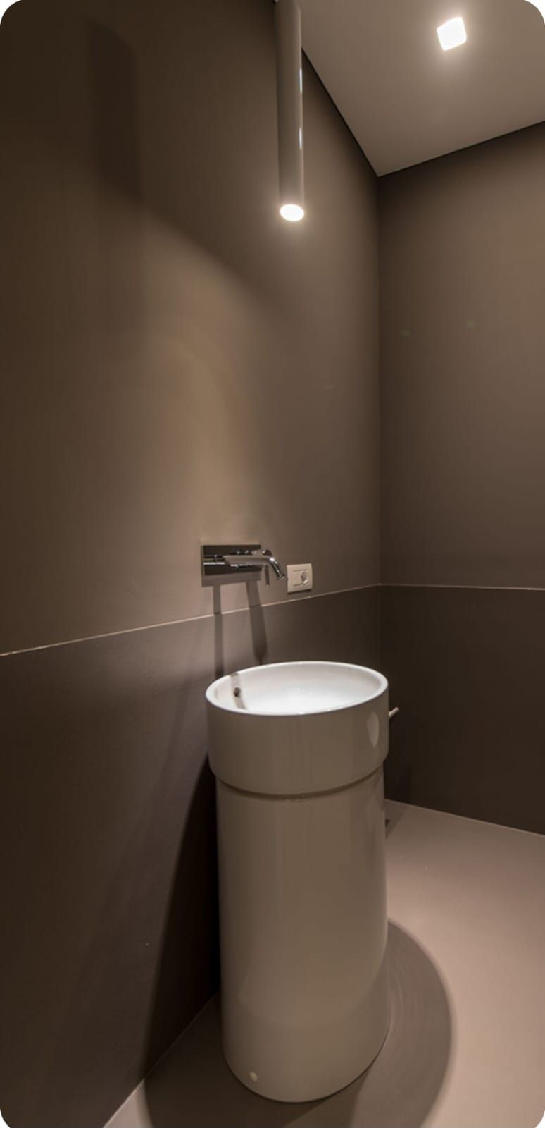 Bagno moderno con WC bianco e pareti marroni illuminate da una luce calda.