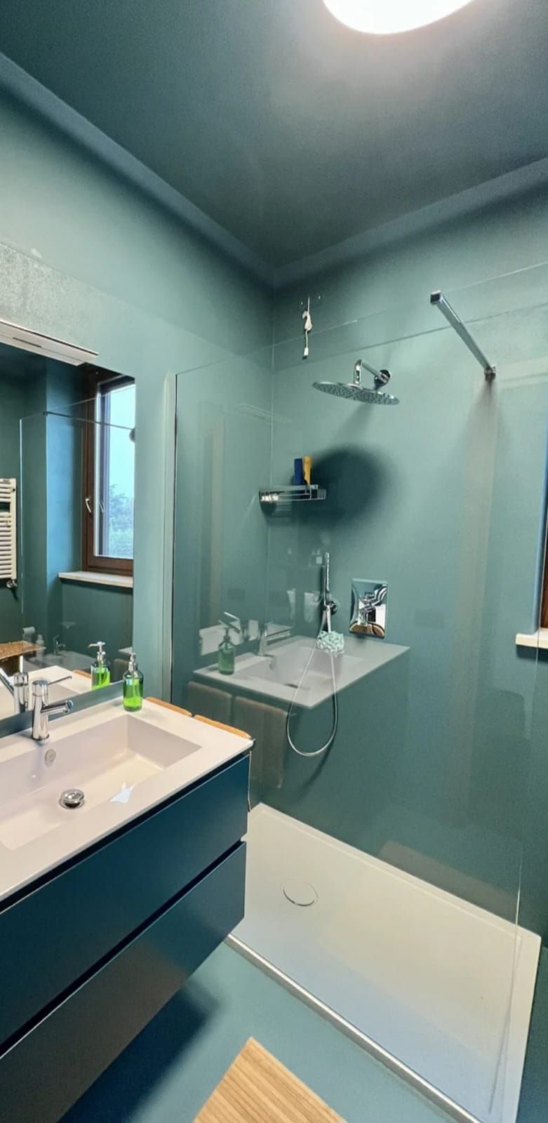 Bagno turchese con lavabo, doccia a parete e piccole mensole, visto dalla porta.