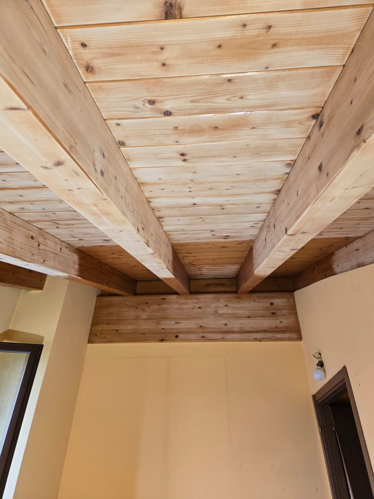 In una stanza stretta, il soffitto è caratterizzato da assi di legno con travi a vista sopra pareti beige.