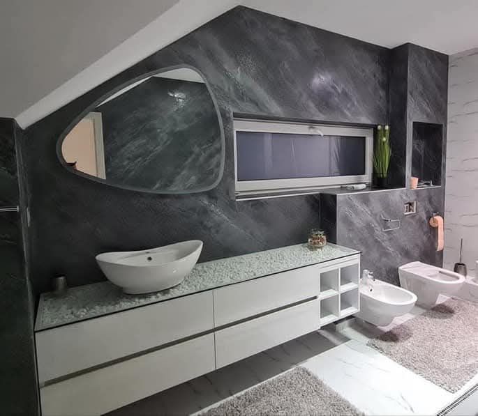 Bagno moderno in bianco e nero con mobile sospeso, lavabo a bacinella, WC, bidet e pareti grigie con finitura materica.