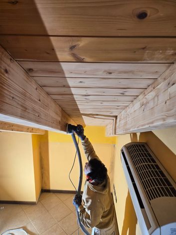 Un operaio utilizza un utensile elettrico per installare pannelli di legno sul soffitto di una stanza gialla.