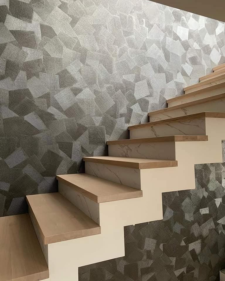 Scala moderna con gradini in legno e rivestimento a parete con motivo geometrico grigio.