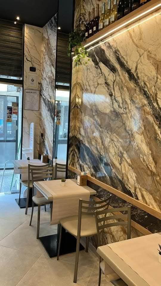 Interno moderno di una caffetteria con parete in marmo, tavolini e sedie vicino a un ingresso in vetro.