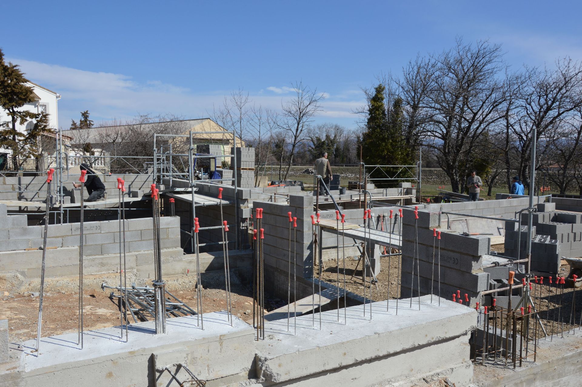Construction site with concrete foundations, rebar, scaffolding, and workers under a clear sky