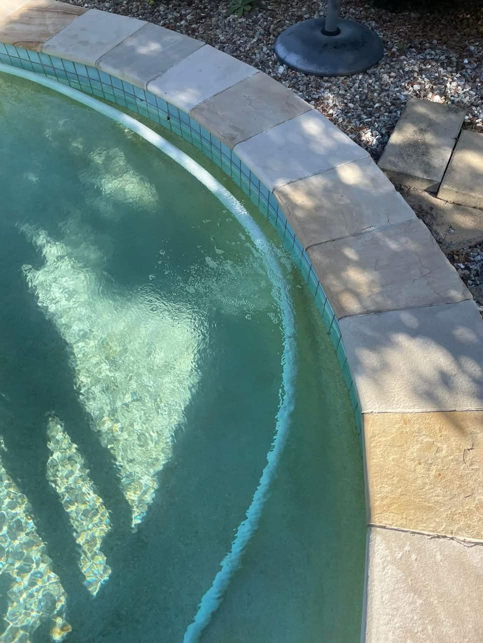 Pool's Edge With Turquoise Water, Beige Stone Border, and Partial View of a Black Umbrella Base — Leak N Pool In Southport, QLD