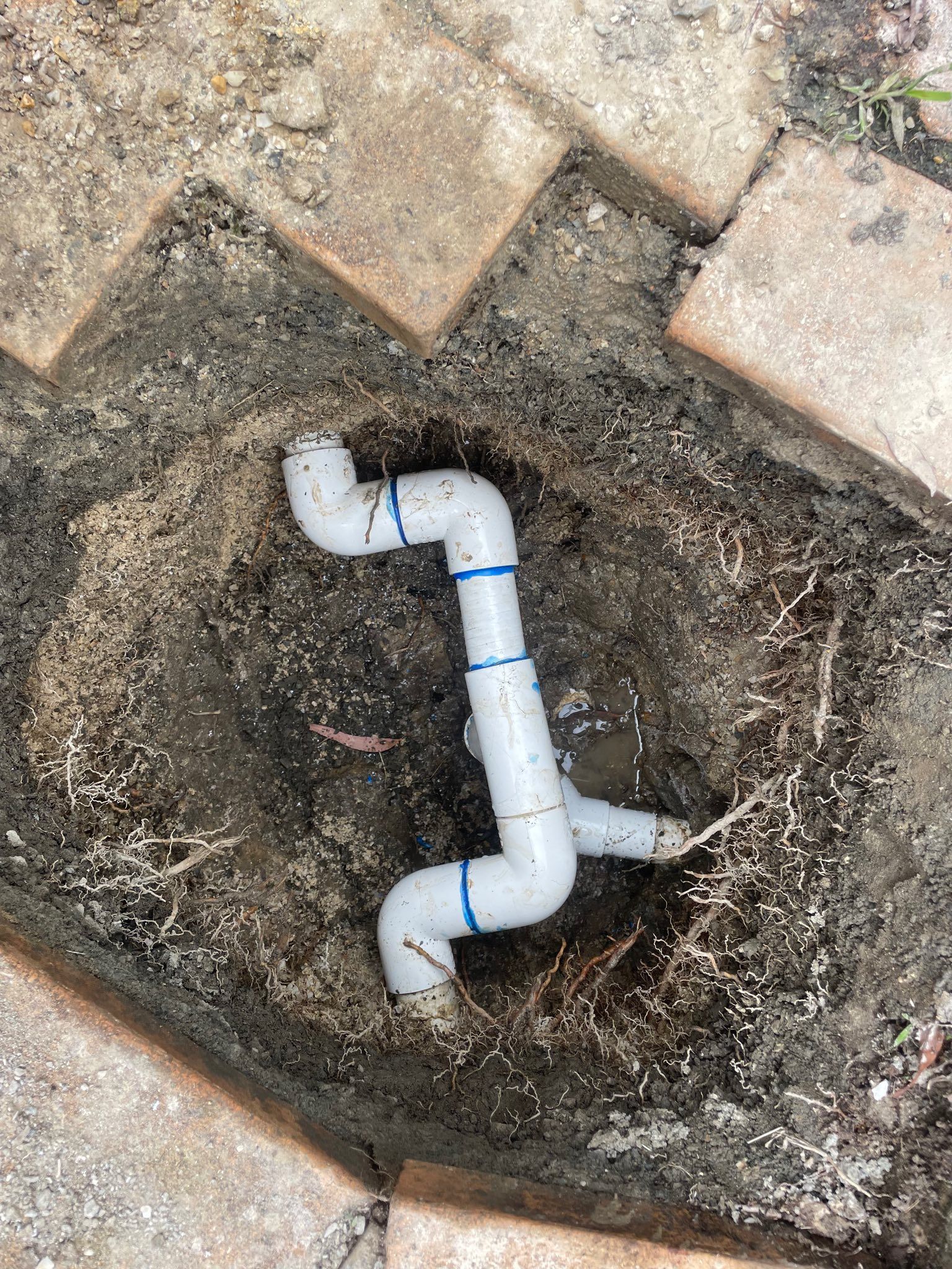 White PVC Pipe Fitting in a Small Hole Surrounded by Dirt and Tan Bricks — Leak N Pool In Southport, QLD