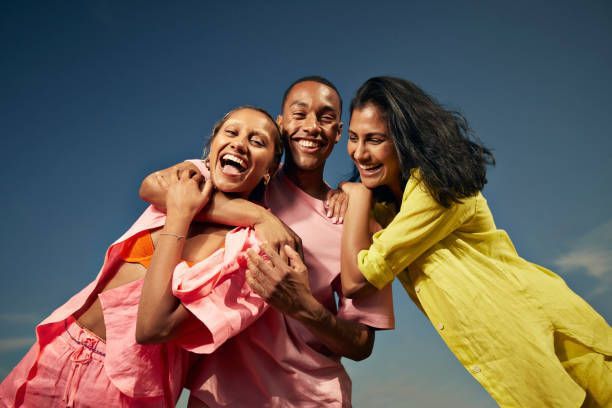 A man and two women are hugging each other in front of a blue sky.