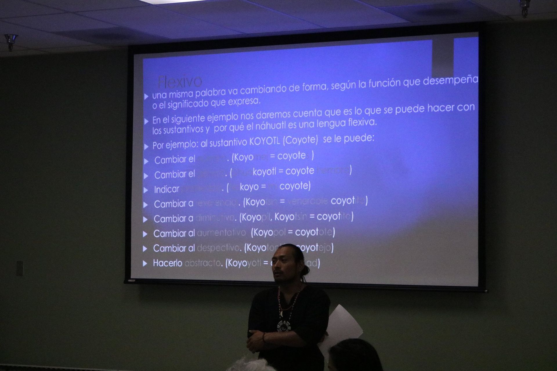 Man presenting a slide with text in a dark room. The slide has blue text on a light blue background.
