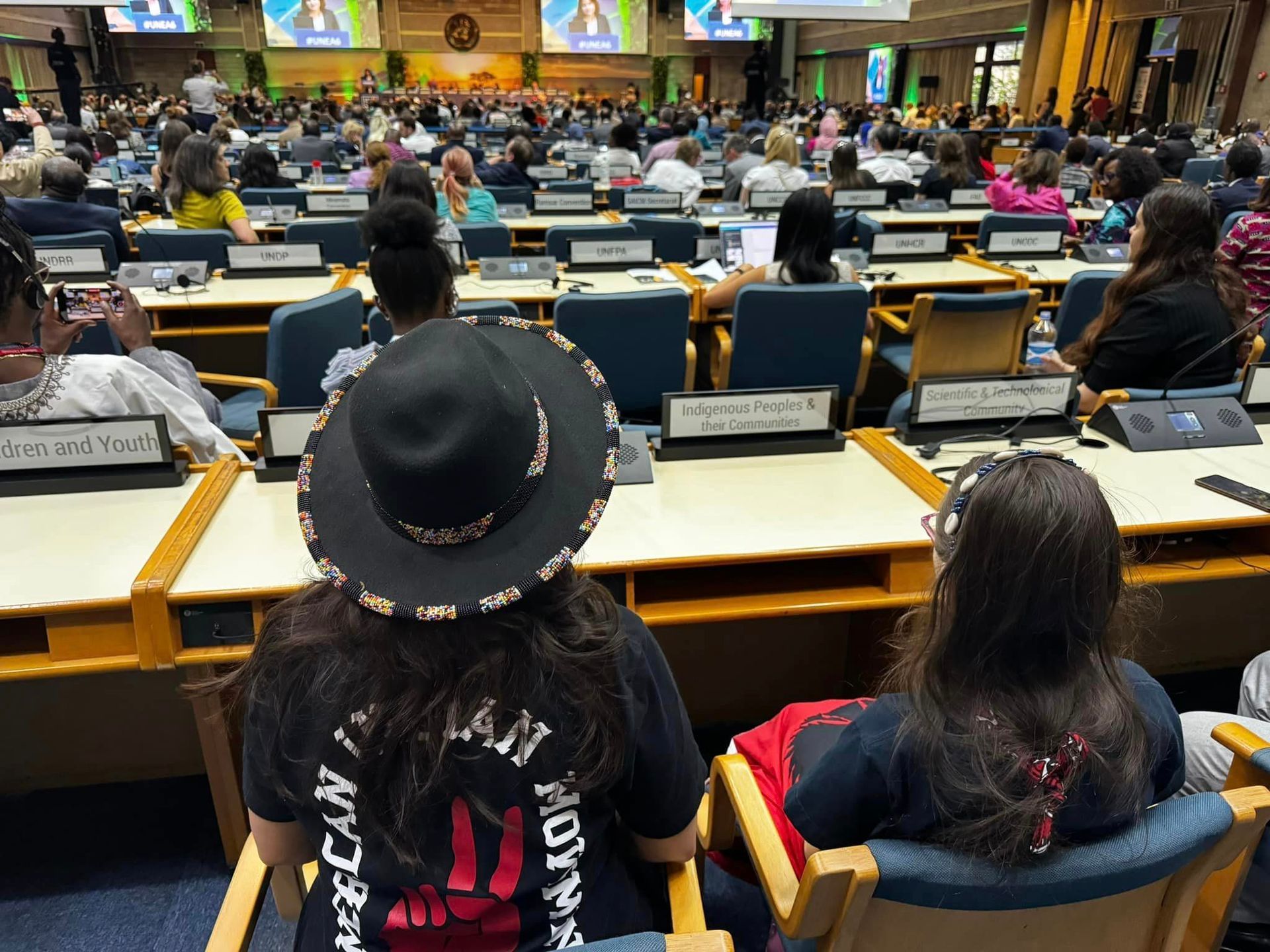 Conference attendees in a large room, many seated, looking toward a speaker.