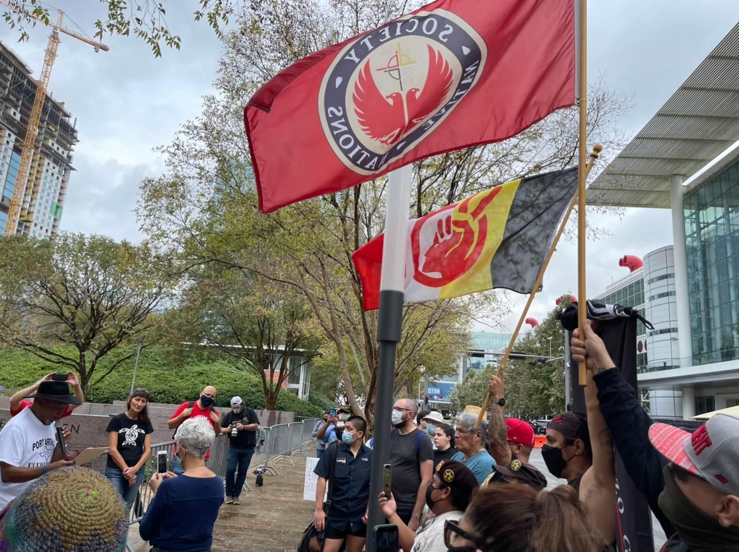 Protesters with flags in front of a building, one flag says 