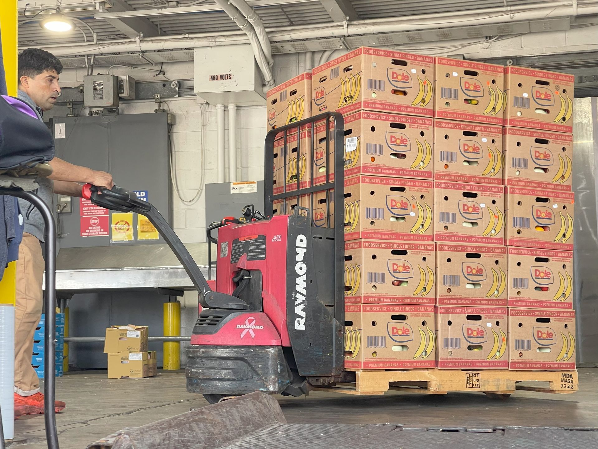 Man operating forklift carrying stacked boxes of bananas in a warehouse.