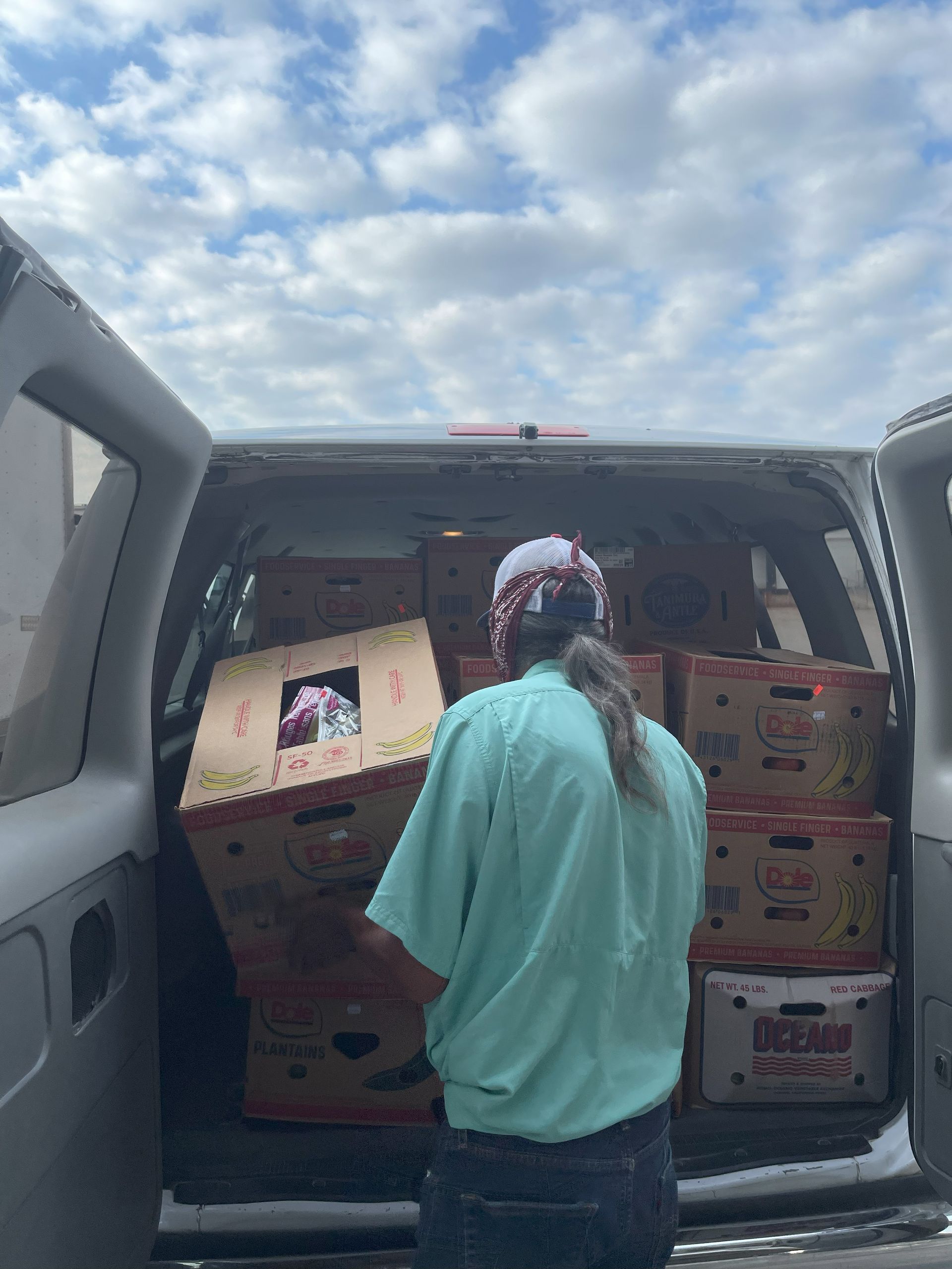 Person loading boxes of food into a van with the doors open, under a cloudy sky.