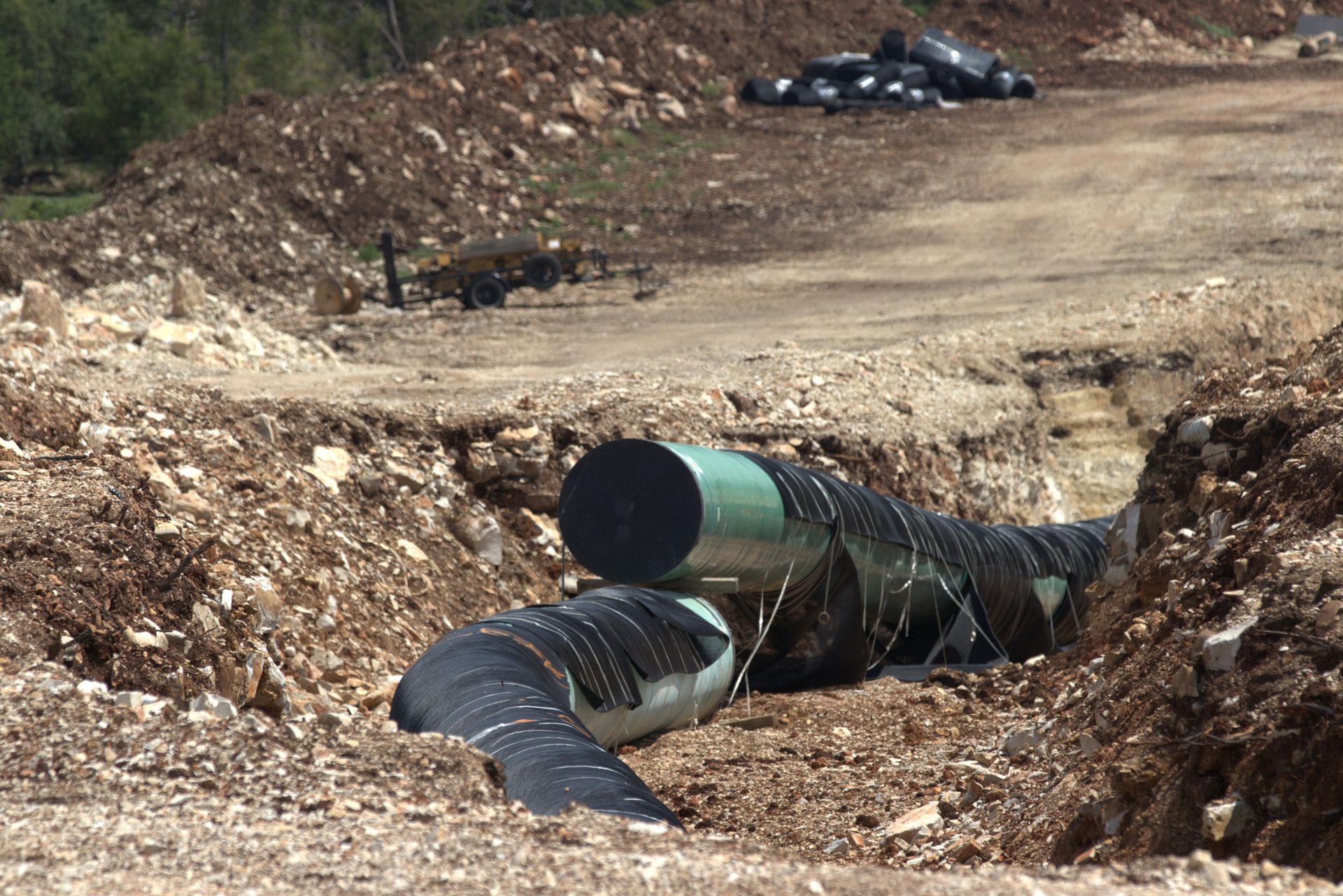 Large pipes being installed in an open trench on a construction site.