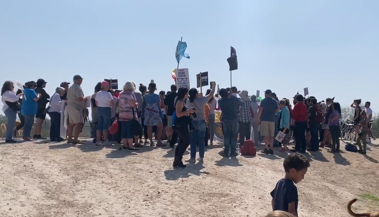 Group of people protesting on a hilltop, holding signs. Clear sky.