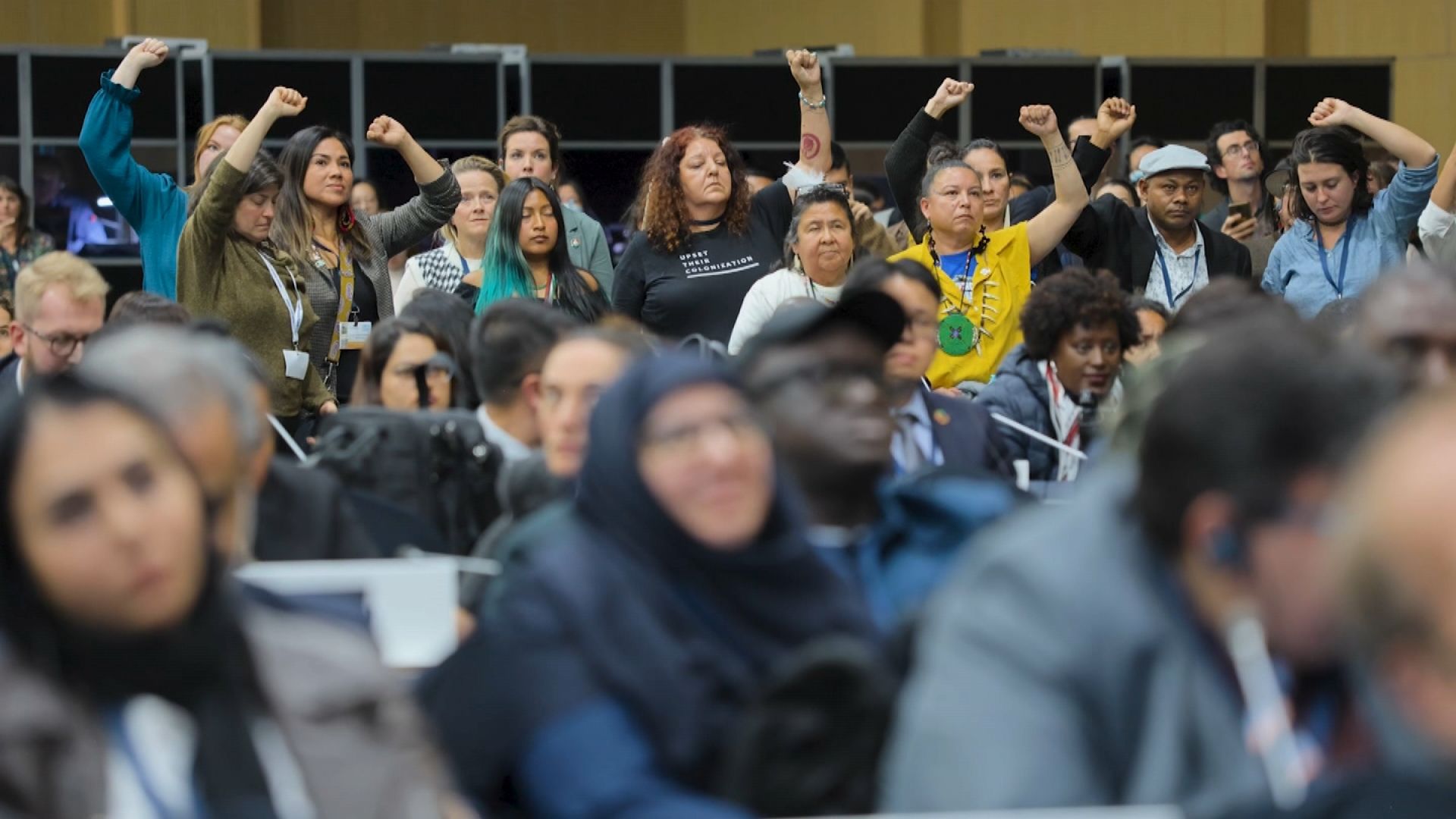 People raising fists at a conference, some looking determined.