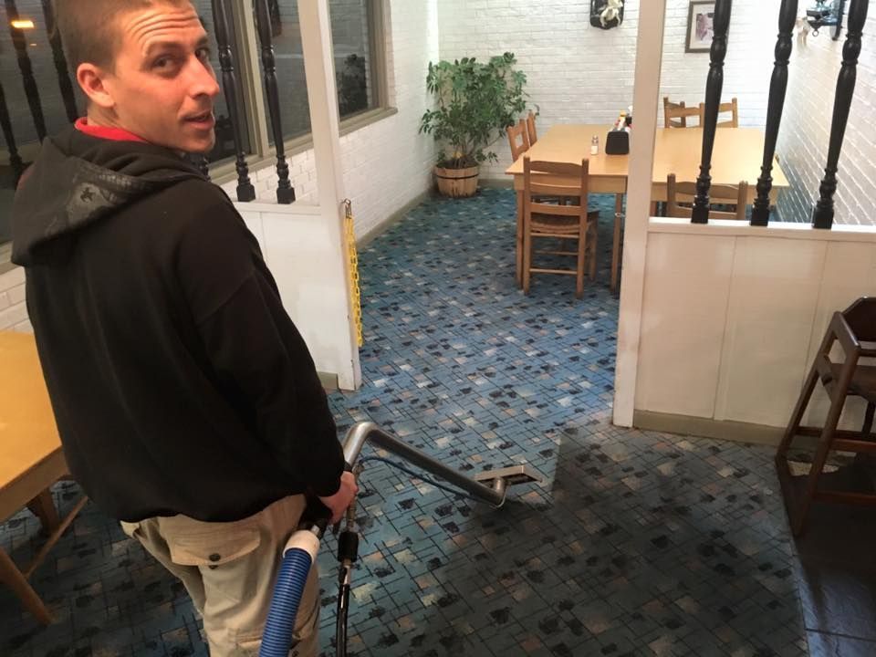 Man in black hoodie looking back in a narrow indoor hallway with blue carpet and tables