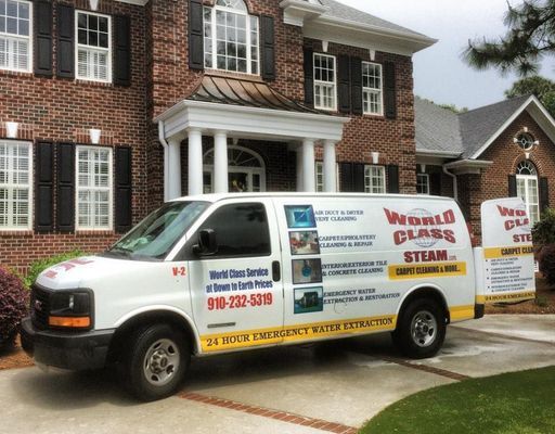 White steam-cleaning van parked in a driveway in front of a brick house