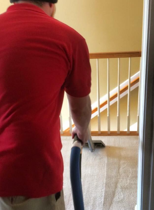 Person vacuuming a carpeted stairway landing in a red shirt.