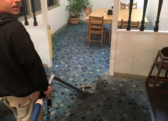 Person holding a vacuum hose in a hallway with blue patterned carpet and a small table in the background