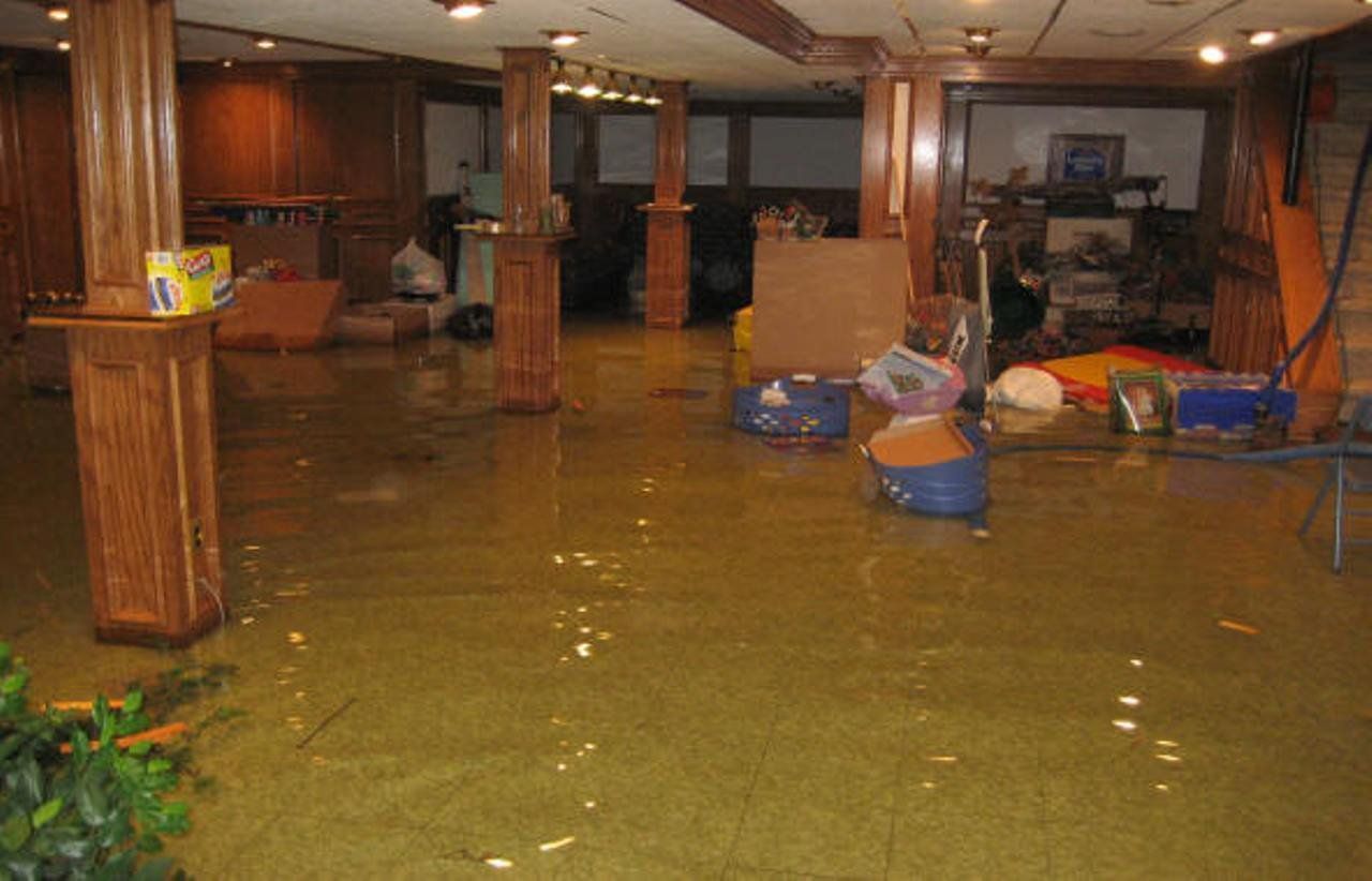 Flooded basement with brown water, columns, and scattered furniture and boxes