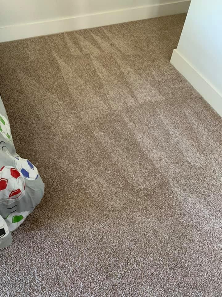 Empty beige carpeted corner with white walls and a patterned fabric bag at the left edge
