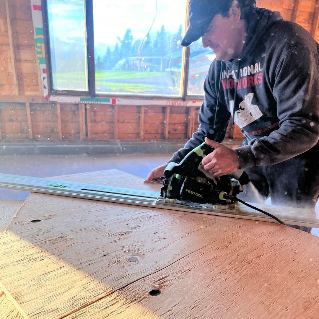A man wearing a national wildlife sweatshirt is cutting a piece of plywood