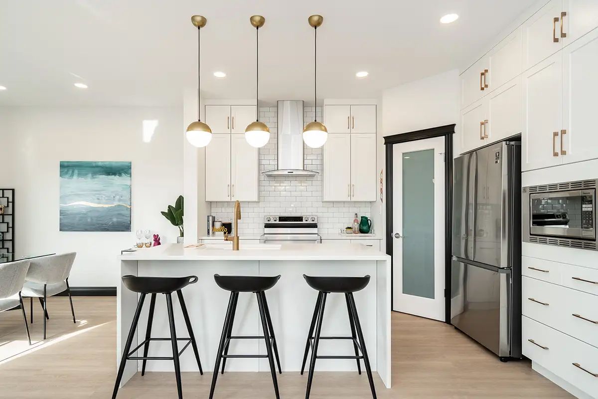 Modern kitchen with white cabinets, island with black stools, and three gold pendant lights.