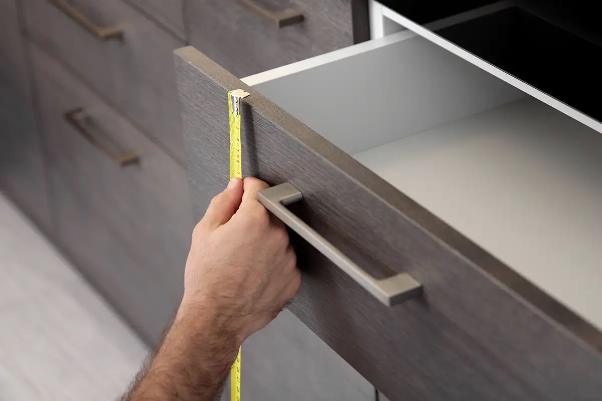 A person is measuring a drawer with a tape measure.
