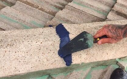 A Person is Using a Spatula to Spread blue Paint on a Concrete Surface — Roof Repairs in Maitland, NSW