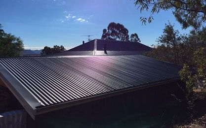 A House with a Black roof and a blue sky in the Background — Roof Repairs in Maitland, NSW