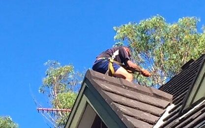 A Man is Sitting on the Roof of a House — Roof Repairs in Maitland, NSW