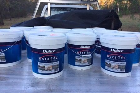 Buckets of Dulux Paint are Sitting on a Table in Front of a Truck — Roof Repairs in Maitland, NSW