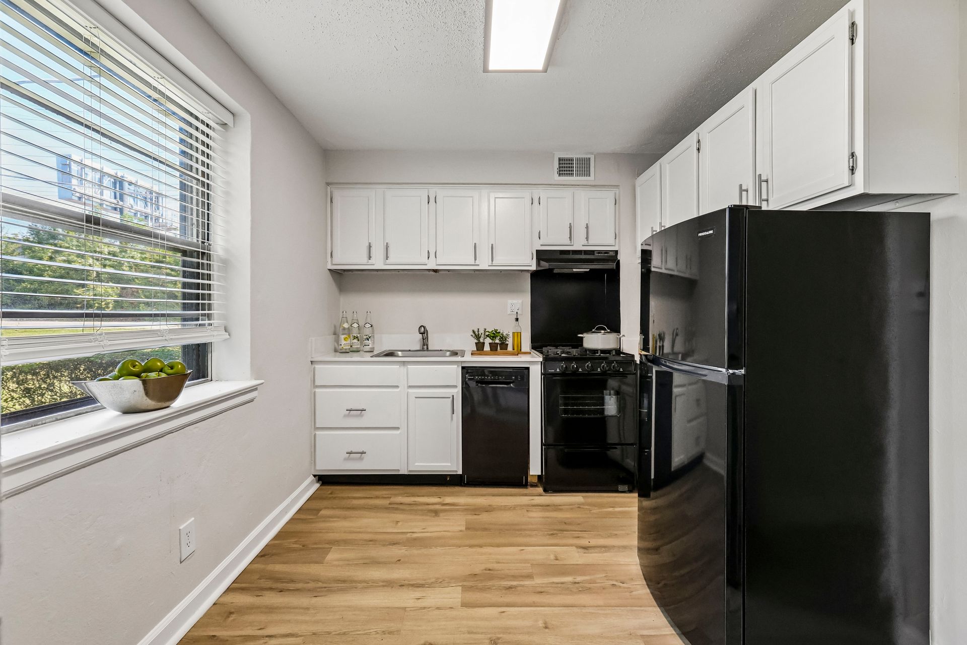 Apartment kitchen with white cabinets, black appliances, and a large window at Brickline Apartments