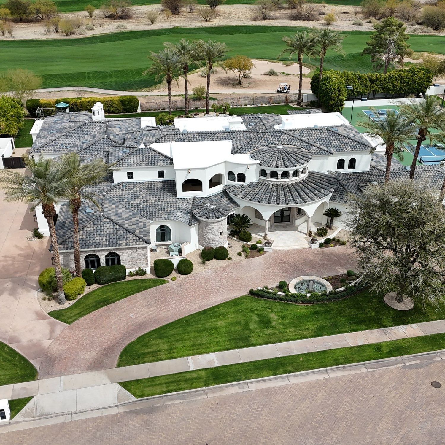 Luxury white home with gray tile roof, palm trees, and green lawn on golf course.