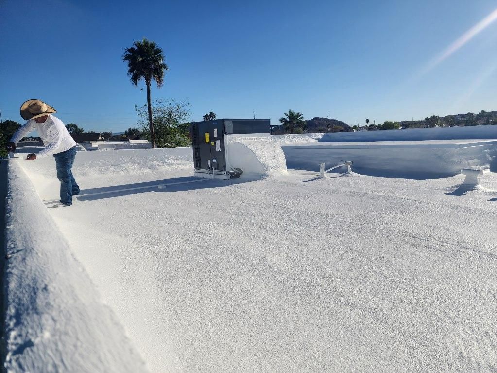 Person on a white roof, reaching towards building equipment, with a palm tree in the background. Clear, sunny sky.