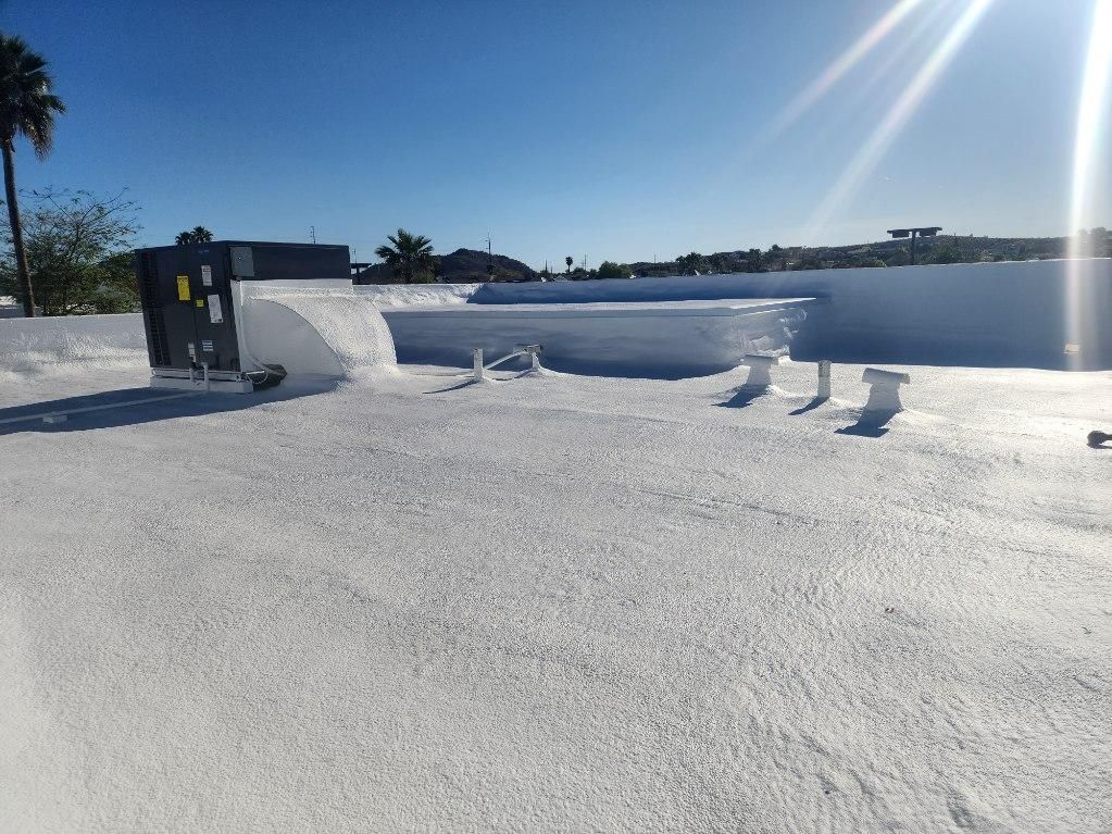 White commercial roof with equipment, against a bright blue sky with sun glare.