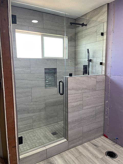 A bathroom with a walk in shower with a glass door and a window.