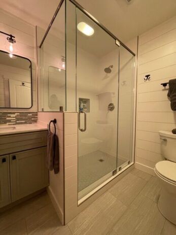 A bathroom with a walk in shower , toilet , sink and mirror.