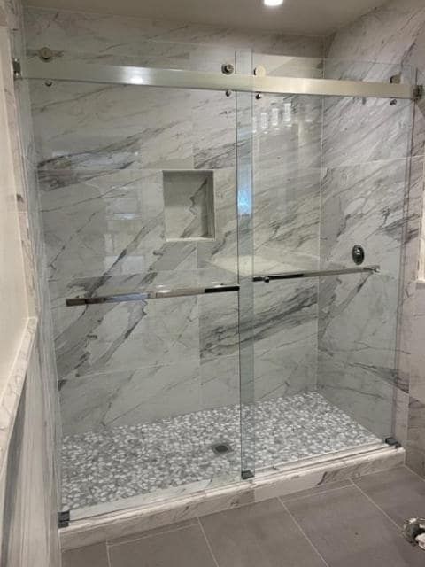 A bathroom with marble walls and a sliding glass shower door.