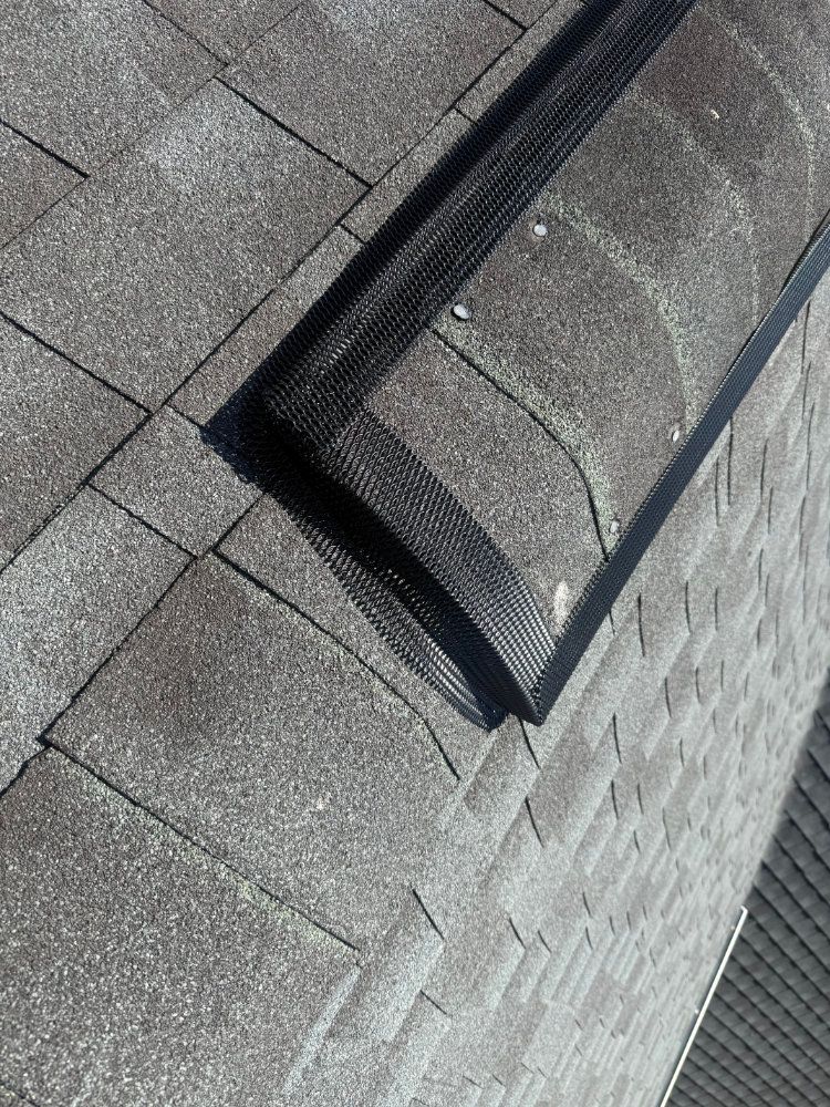 Close-up of a roof with gray shingles and a black vent or skylight trim.