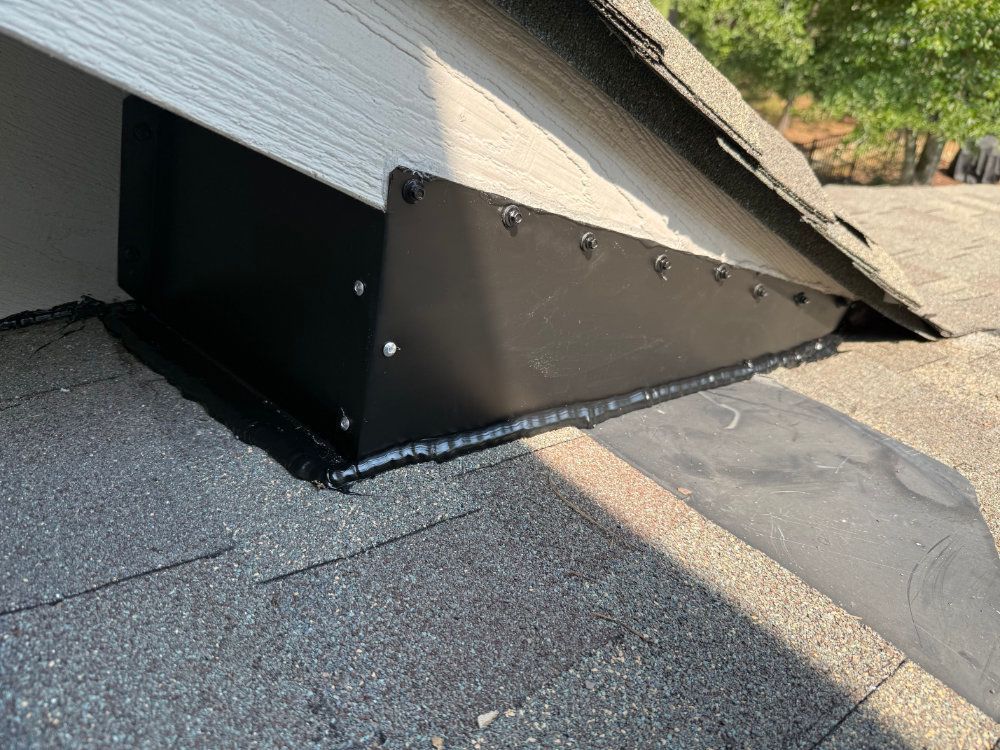 Black roof vent or attic exhaust hood on a shingled roof with metal flashing and rivets